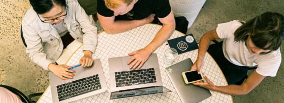 people sitting at a desk with laptops in front of them