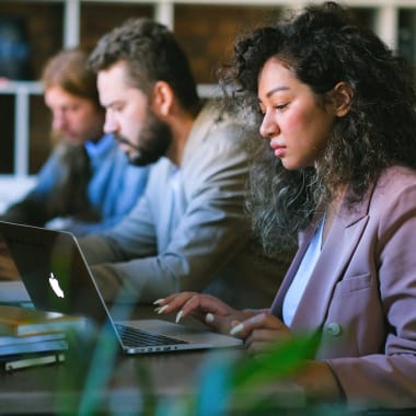 three people sitting at a desk in front of laptops