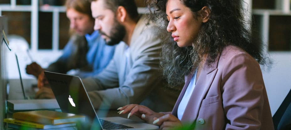 three people sitting at a desk in front of laptops