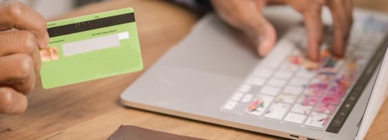 A hand holding a credit card and typing on laptop